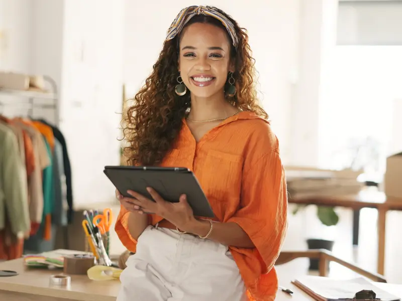 Pessoa sorrindo e segurando um tablet em um ambiente de loja de roupas, representando o suporte contábil para microempreendedores.